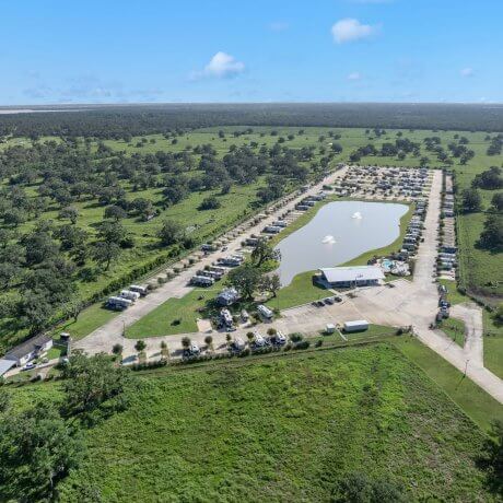 An aerial view of paved roads and RV sites that are spacious and surrounded by lush scenery and gated comfort at Brazoria Lakes RV Resort in Brazoria, TX.